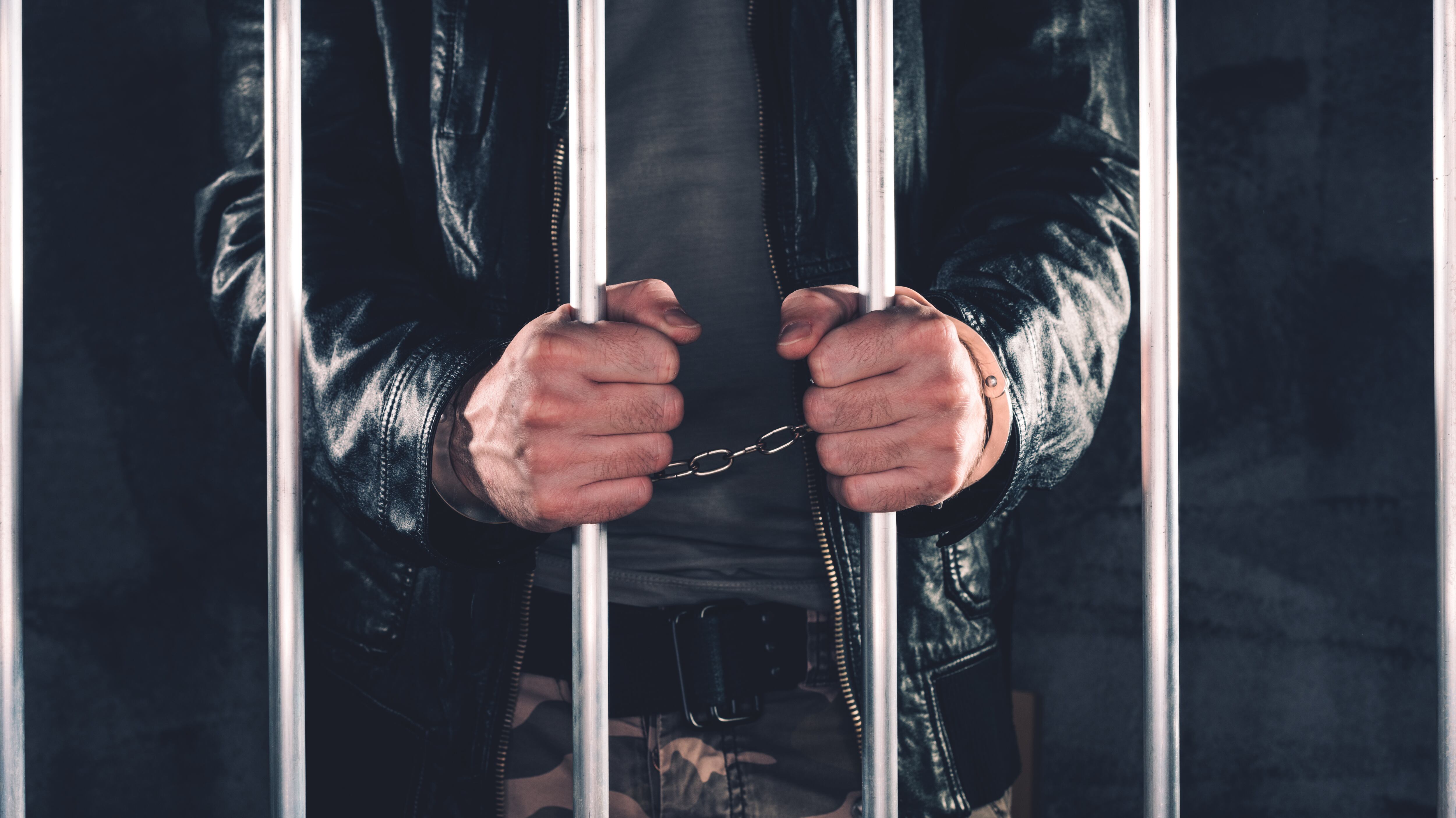 Handcuffed man behind prison bars. Arrested criminal male person imprisoned.