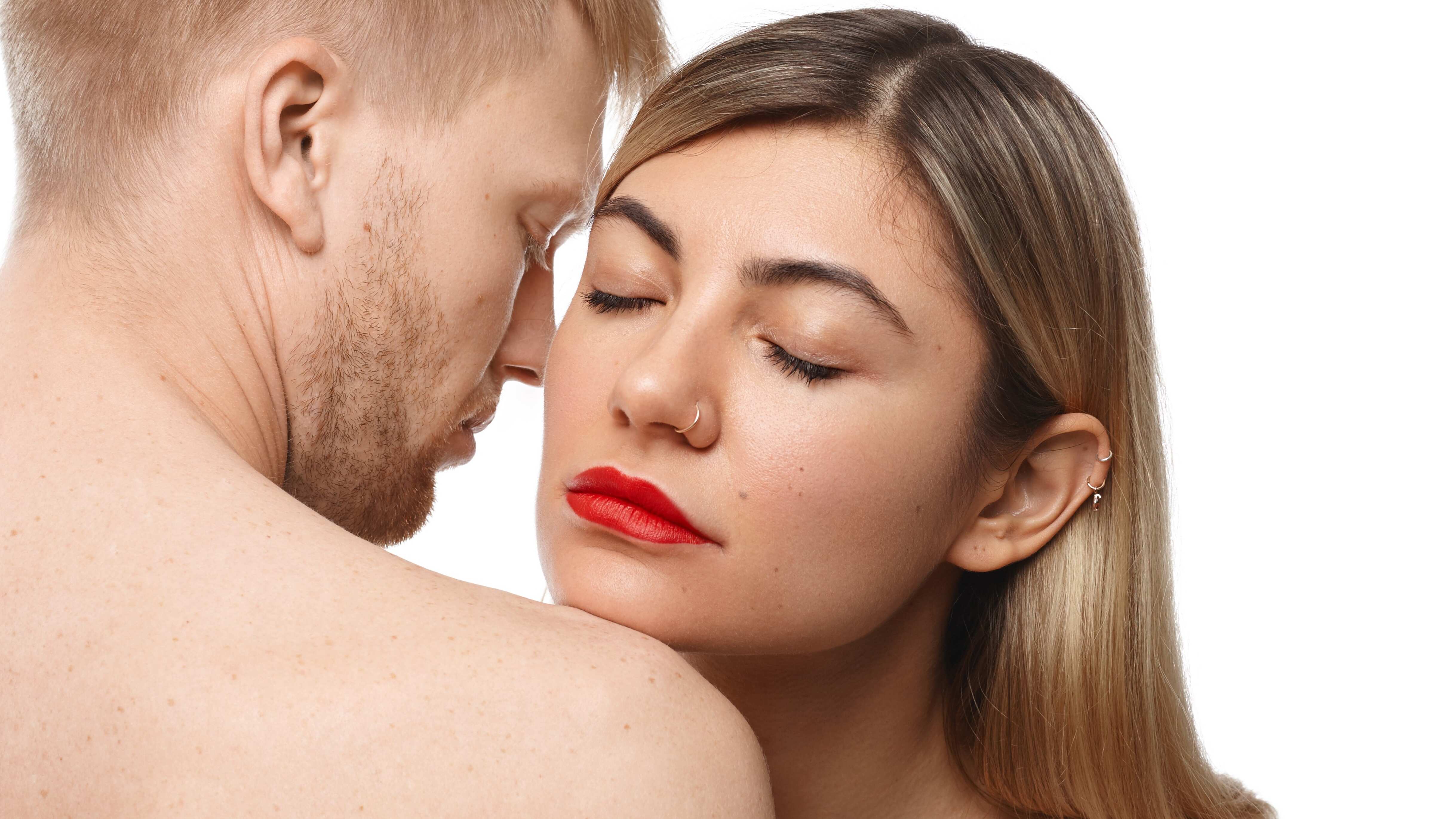 Mulher branca de batom vermelho cheirando pescoço de homem branco loiro sem camisa