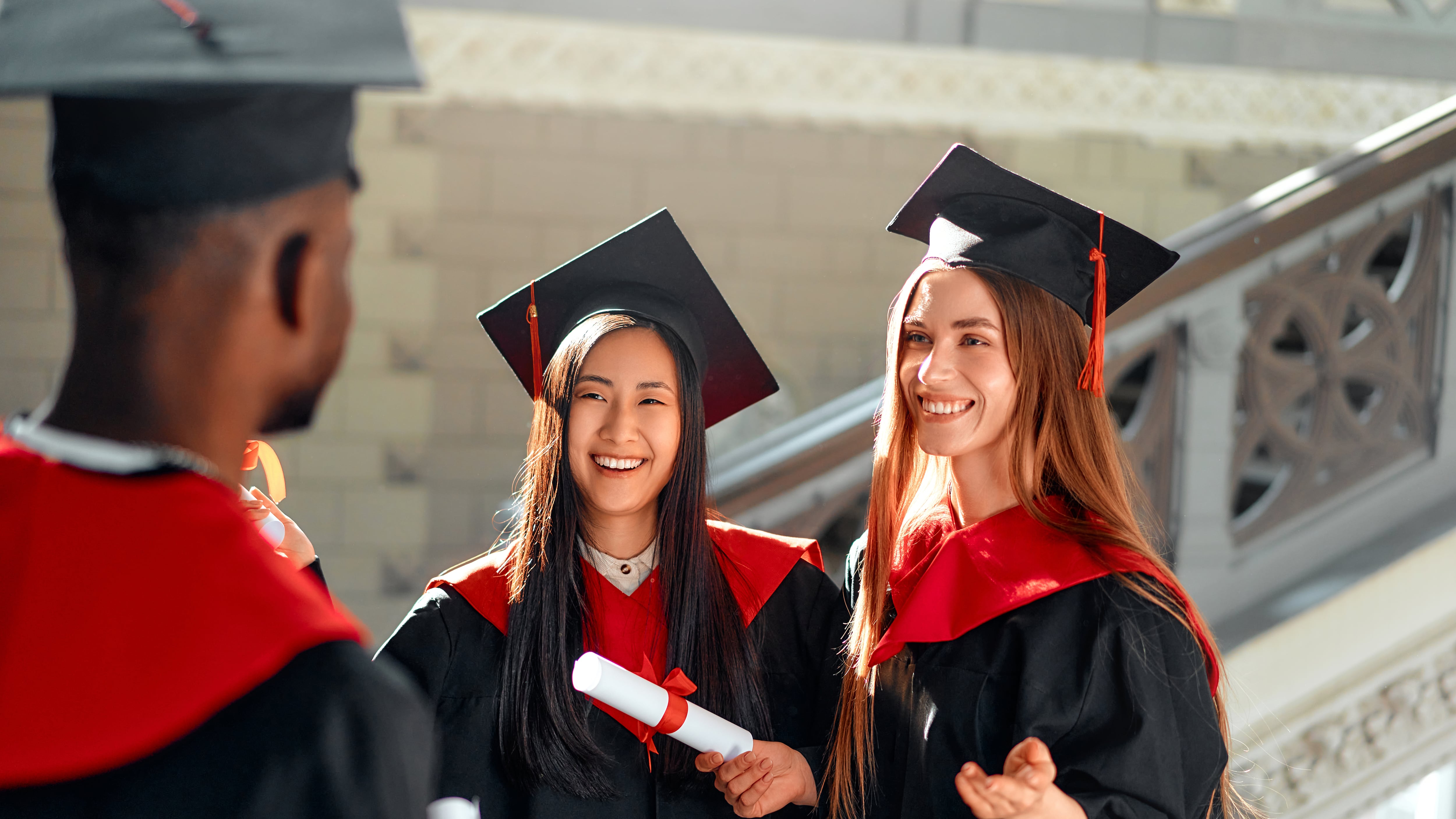 Diverse group of happy students in graduation gowns and caps celebrate academic achievements with smiles at joyful ceremony, bonding and sharing congratulations during milestone success