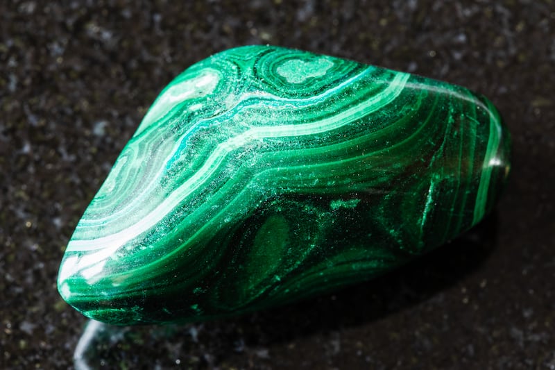 sample of polished malachite mineral on black granite background close up from Congo