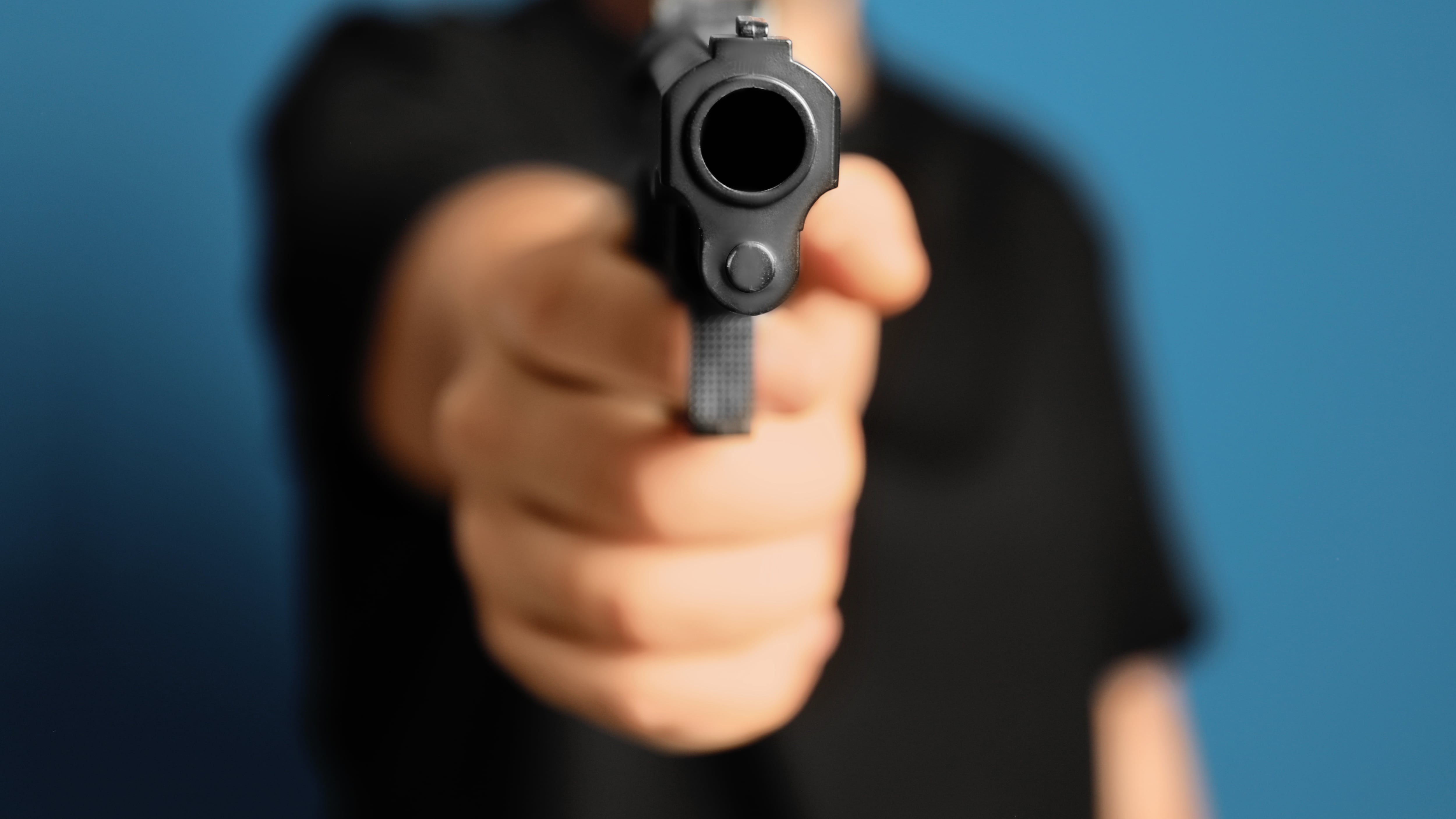 Hombre con pistola sobre fondo azul, primer plano