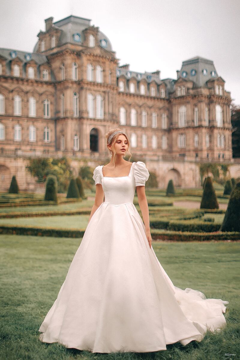 El famoso cuento de hadas de Cenicienta comienza con un único deseo, un vestido exquisito y el sueño de su vida. Y creemos que toda la esperanza y la magia de su historia se reflejan en este extraordinario vestido de gala de Mikado: un vestido realmente exquisito. Cuentas perladas adornan el escote cuadrado del vestido, que se combina con un conjunto de pintorescas mangas abullonadas desmontables, mientras que la cintura vasca de nuestro look inspirado en la Cenicienta de Disney conduce a una impresionante cola con volantes.