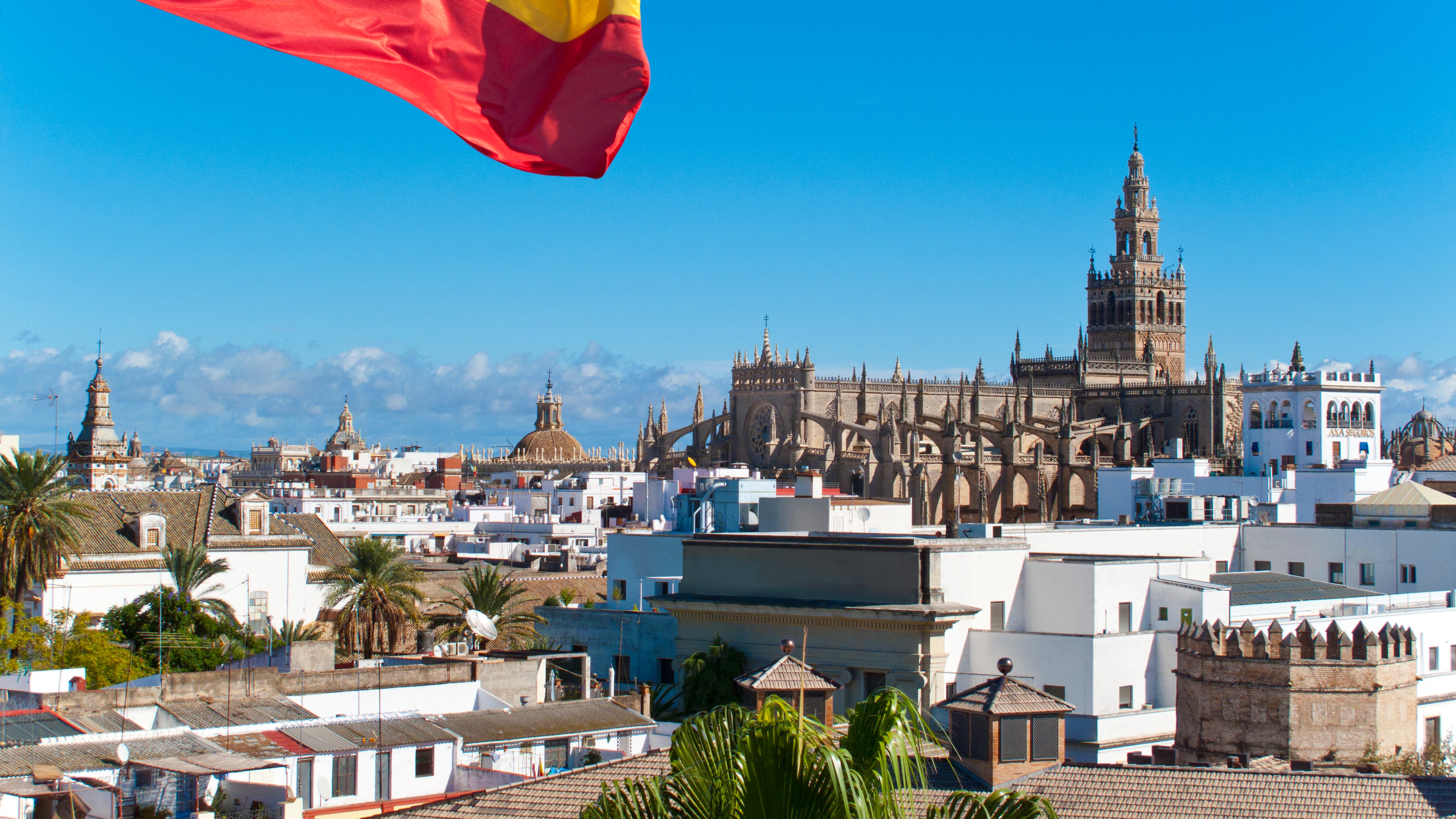 Bandera española ondeando con la catedral de fondo, Sevilla, España