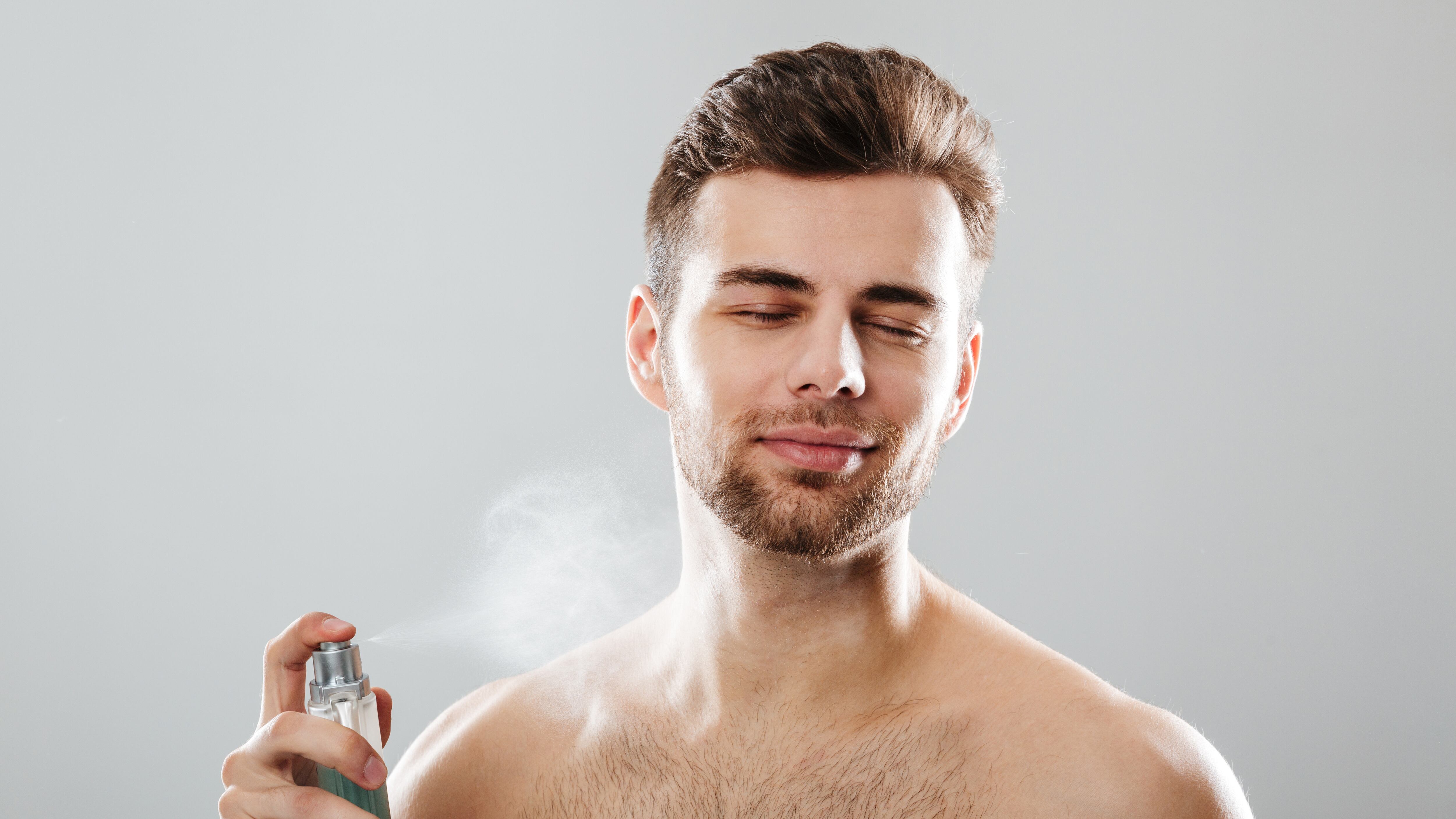 Homem branco sem camiseta borrifando perfume