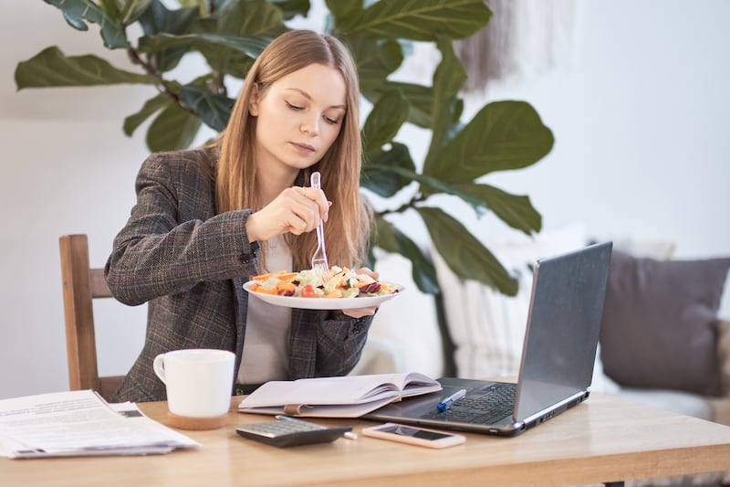 Mujer de negocios sentada con una computadora portátil en un café y desayunando con una taza de café.