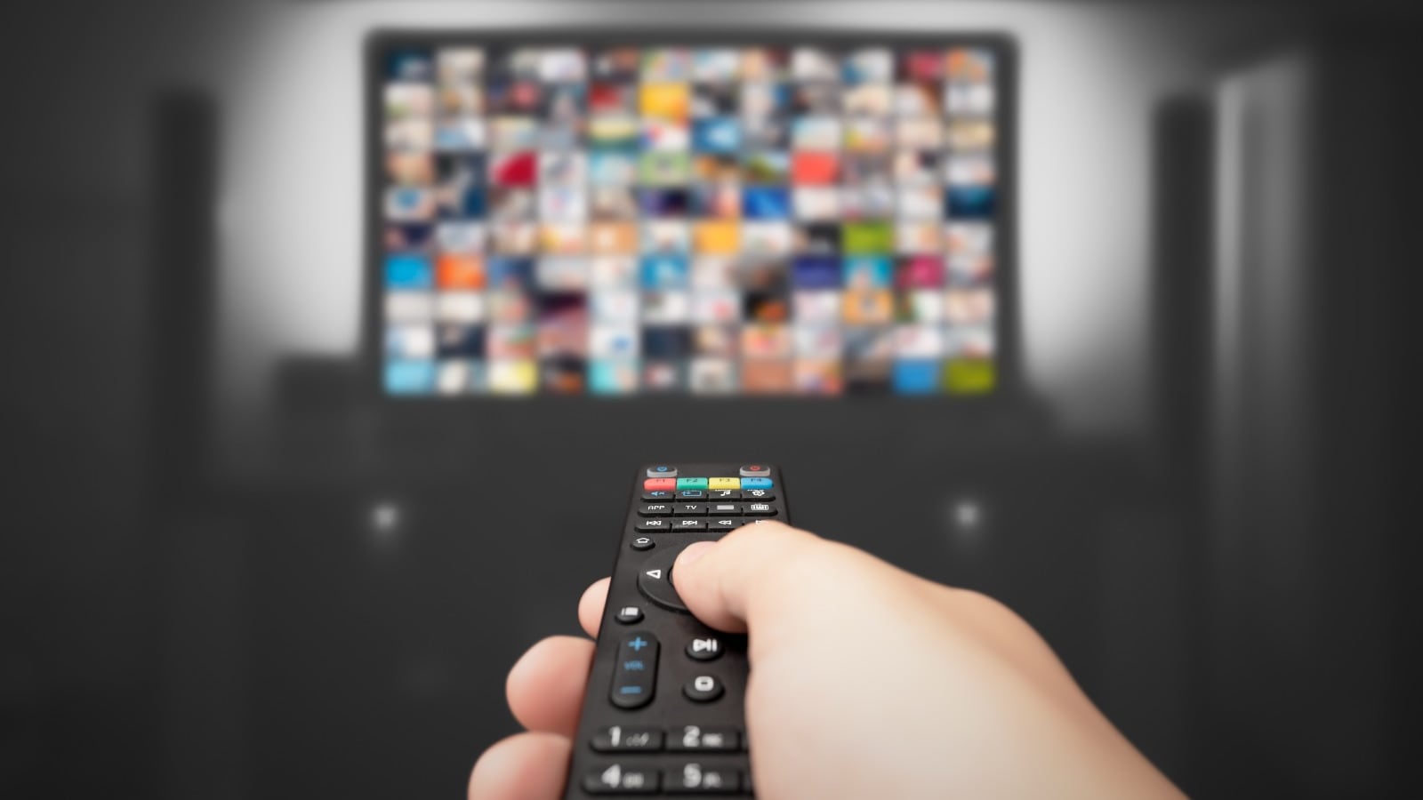 Una mano apunta un control remoto hacia un televisor, en el que se observan cuadritos borrosos simulando diferentes escenas o aplicaciones.
