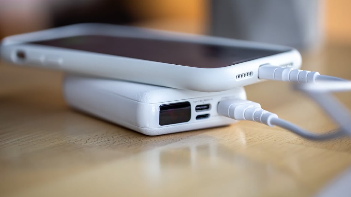 El teléfono inteligente se carga desde un pequeño banco de energía blanco a través de un cable, de cerca