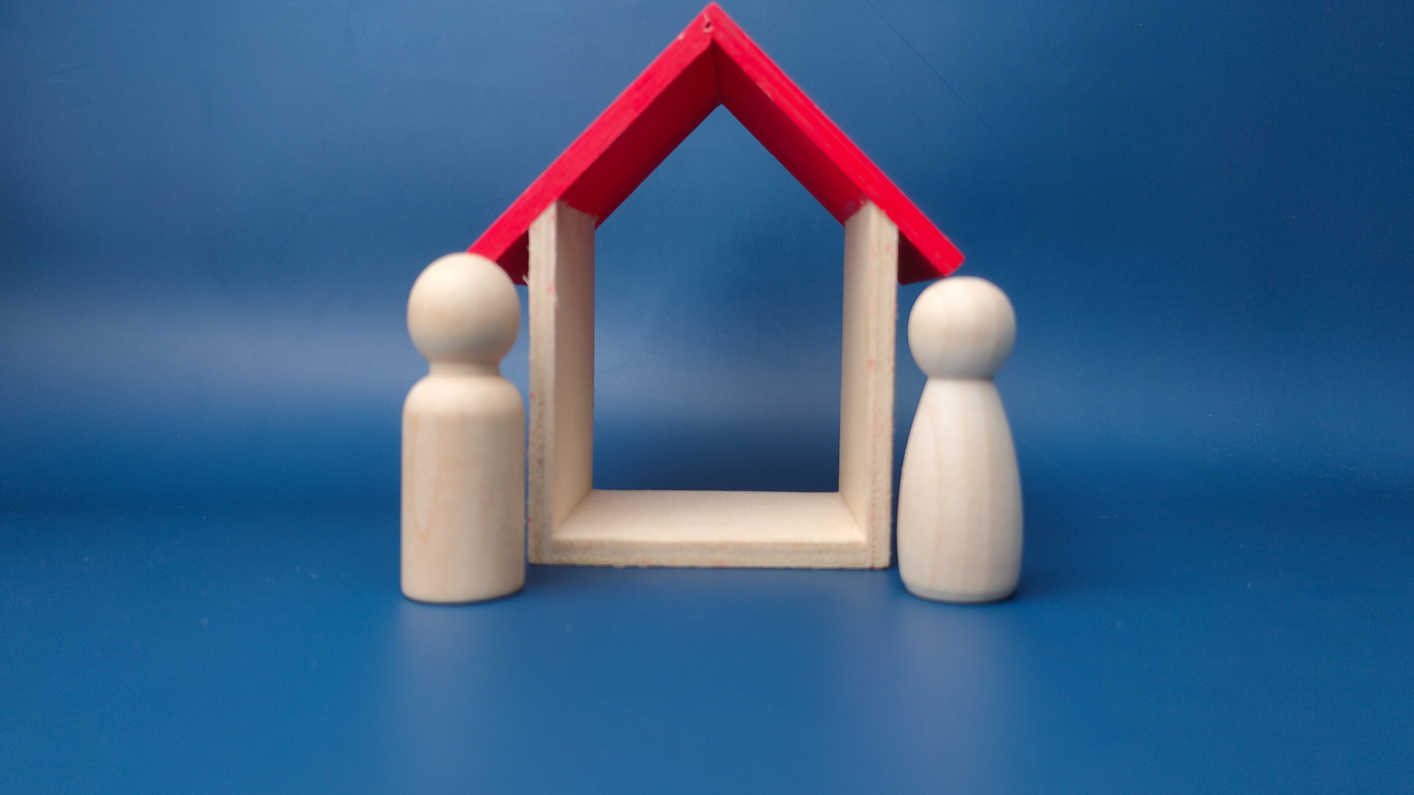 Una pareja de muñecas de madera con casa de madera sobre fondo azul.